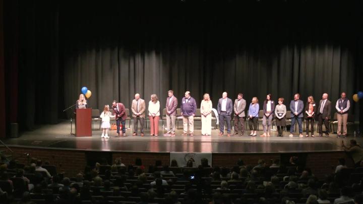 A line of people stand on the stage as they wait to shake a little girls hand. 
