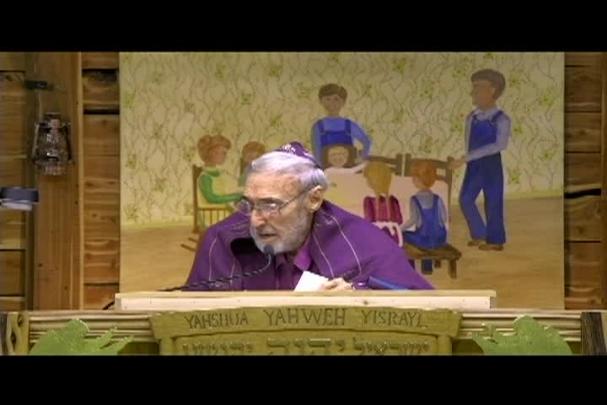 A man sitting center with a cloth behind him depicting a family sitting at a table. 