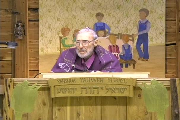 A man sitting center with a cloth behind him depicting a family sitting at a table. 