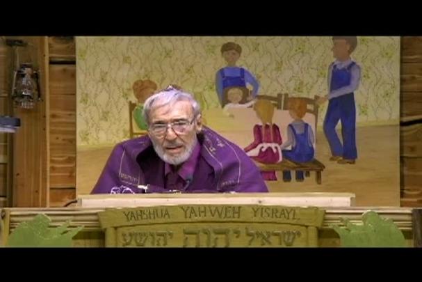 A man sitting center with a cloth behind him depicting a family sitting at a table. 