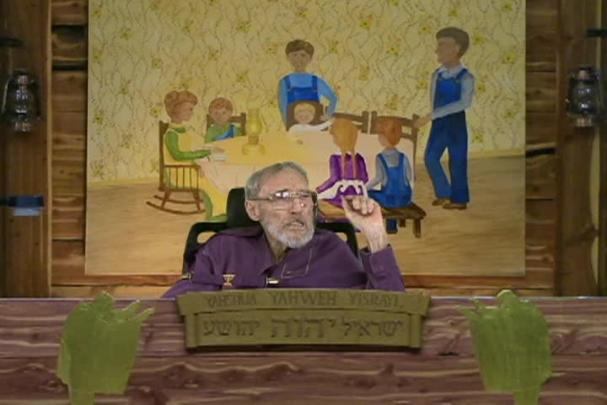 A man sitting center with a cloth behind him depicting a family sitting at a table. 