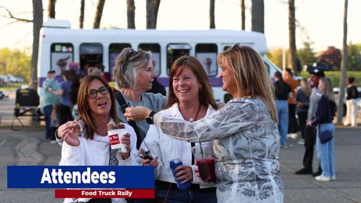 A group of women stand in front a food truck. The woman on the far right is holding a lavaliere microphone and holding it next tot he woman on the left. 