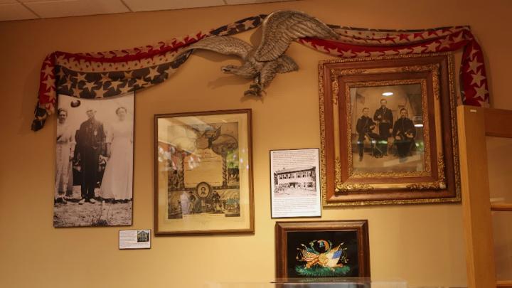 A collection of artifacts hung on the wall with an American flag theme cloth dangled above hanging on a plaque on a eagle. 