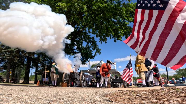 A cloud of smoke drifts form a canon with an American flag waving to the right. 