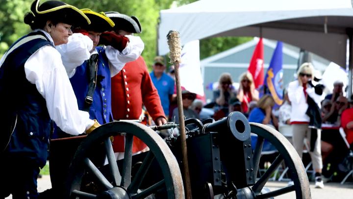 People dressed in patriotic wear prepare to fire a canon. 