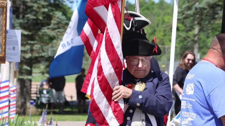 A man dressed in Revolutionary War wear carries an American Flag. 